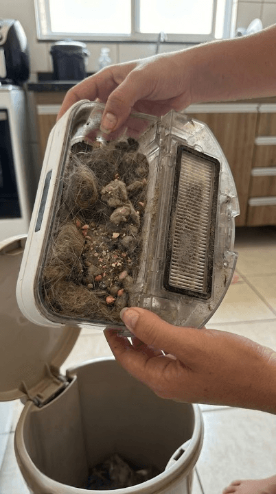 Isabelle segurando o compartimento de pó do robô aspirador lotado de sujeira e pelos